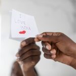 Black Female Hand Putting Sticky Note With Love Message On Mirror, Closeup
