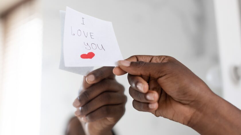 Black Female Hand Putting Sticky Note With Love Message On Mirror, Closeup