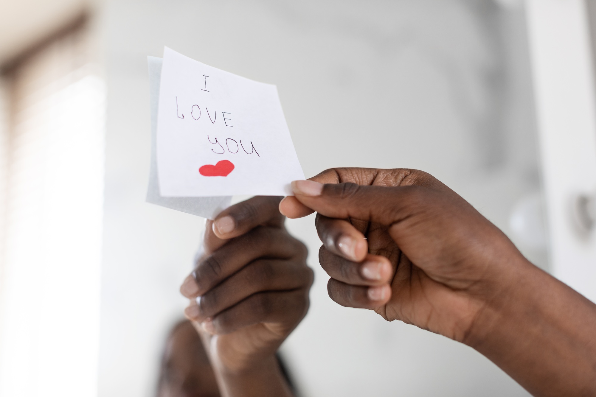Black Female Hand Putting Sticky Note With Love Message On Mirror, Closeup