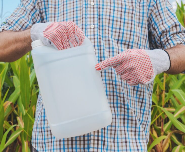 Farmer holding pesticide chemical jug in cornfield
