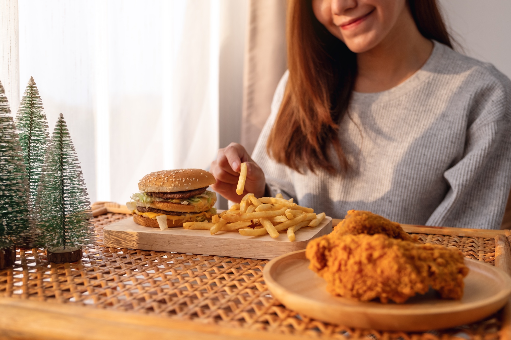 woman holding and eating french fries and hamburger with fried chicken on the table at home