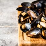 A bunch of boiled mussels on a wooden cutting board.