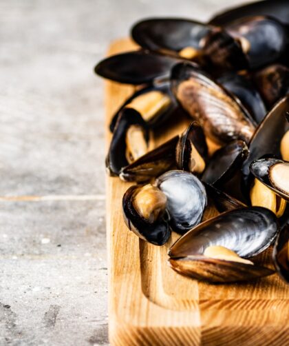 A bunch of boiled mussels on a wooden cutting board.