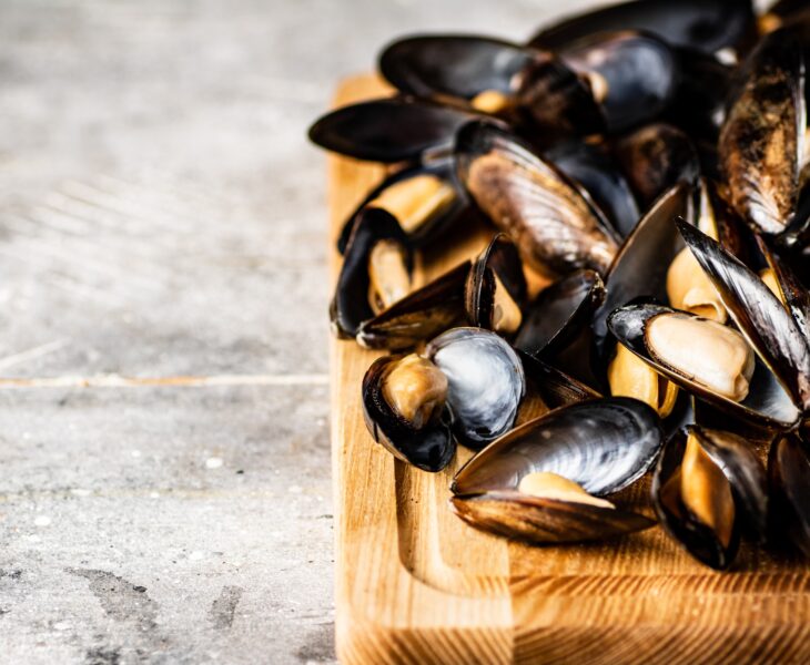 A bunch of boiled mussels on a wooden cutting board.