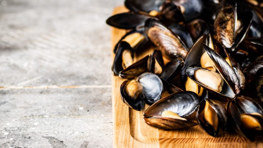 A bunch of boiled mussels on a wooden cutting board.