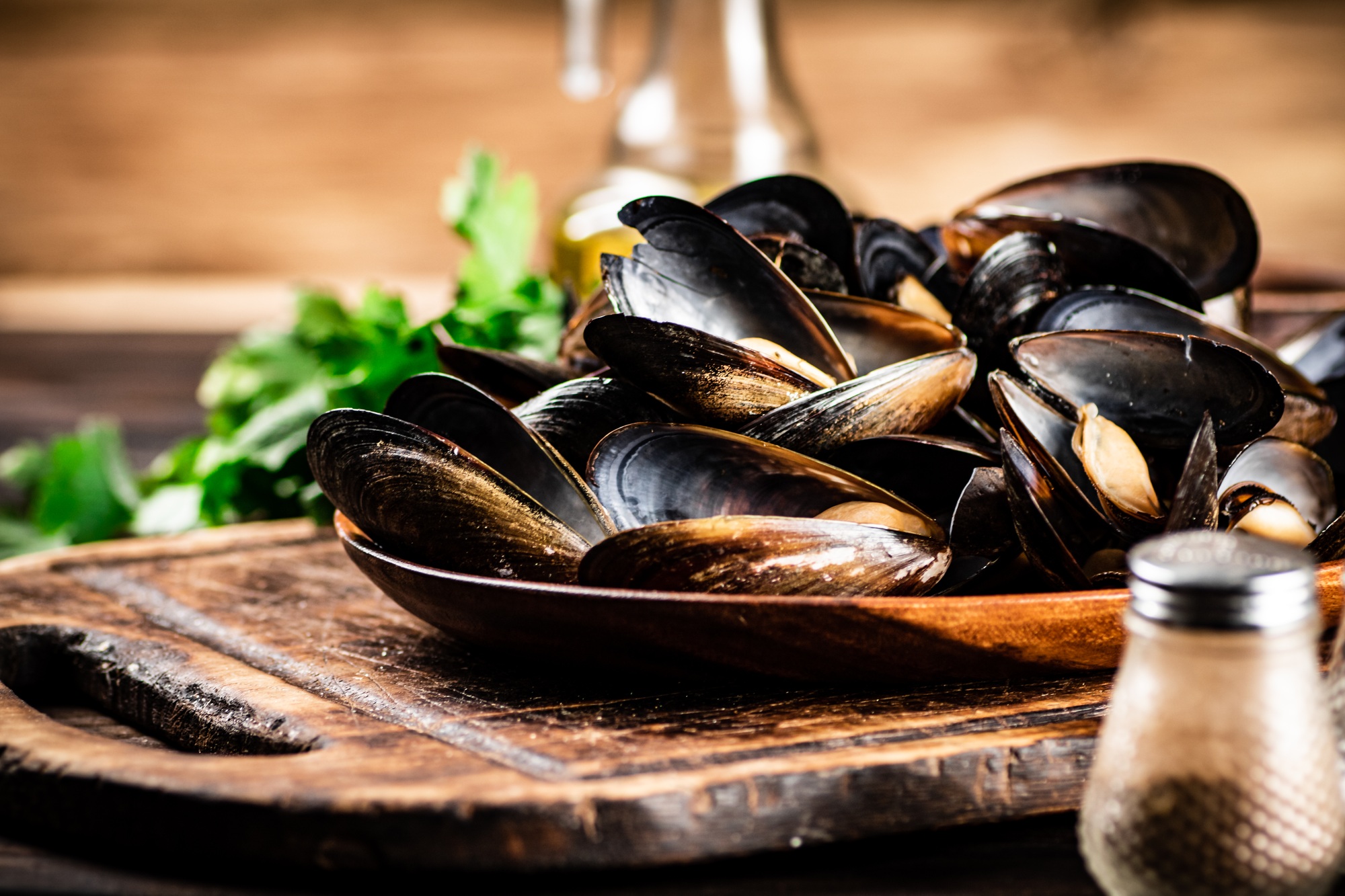 Boiled mussels in a plate on a cutting board with parsley and spices.