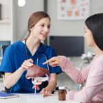 Caucasian liver professional female doctor explain to asian female patient using human liver model