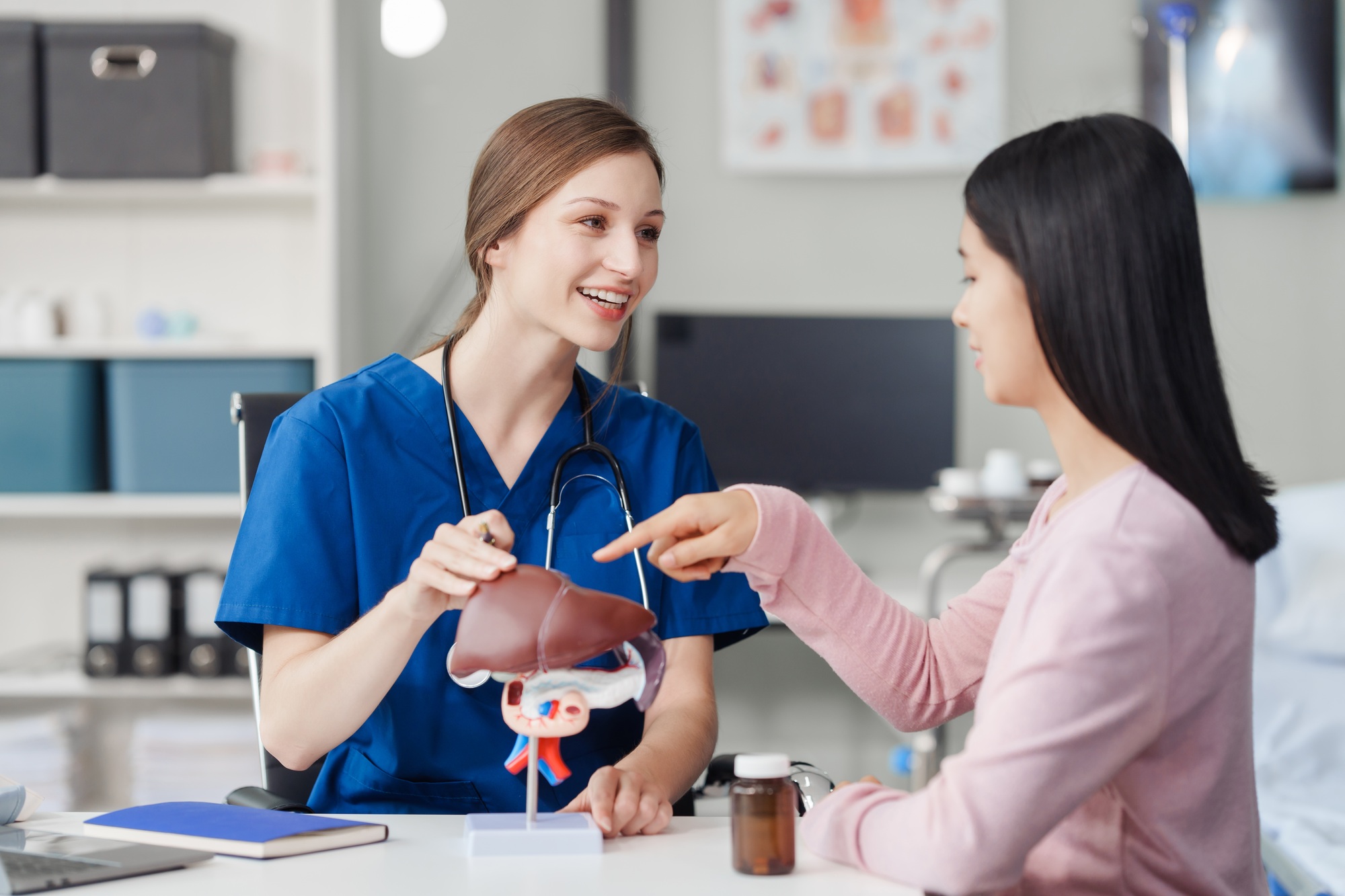 Caucasian liver professional female doctor explain to asian female patient using human liver model
