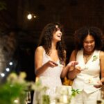 Cheerful young lesbian brides in wedding attire spreading cake among guests