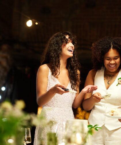 Cheerful young lesbian brides in wedding attire spreading cake among guests