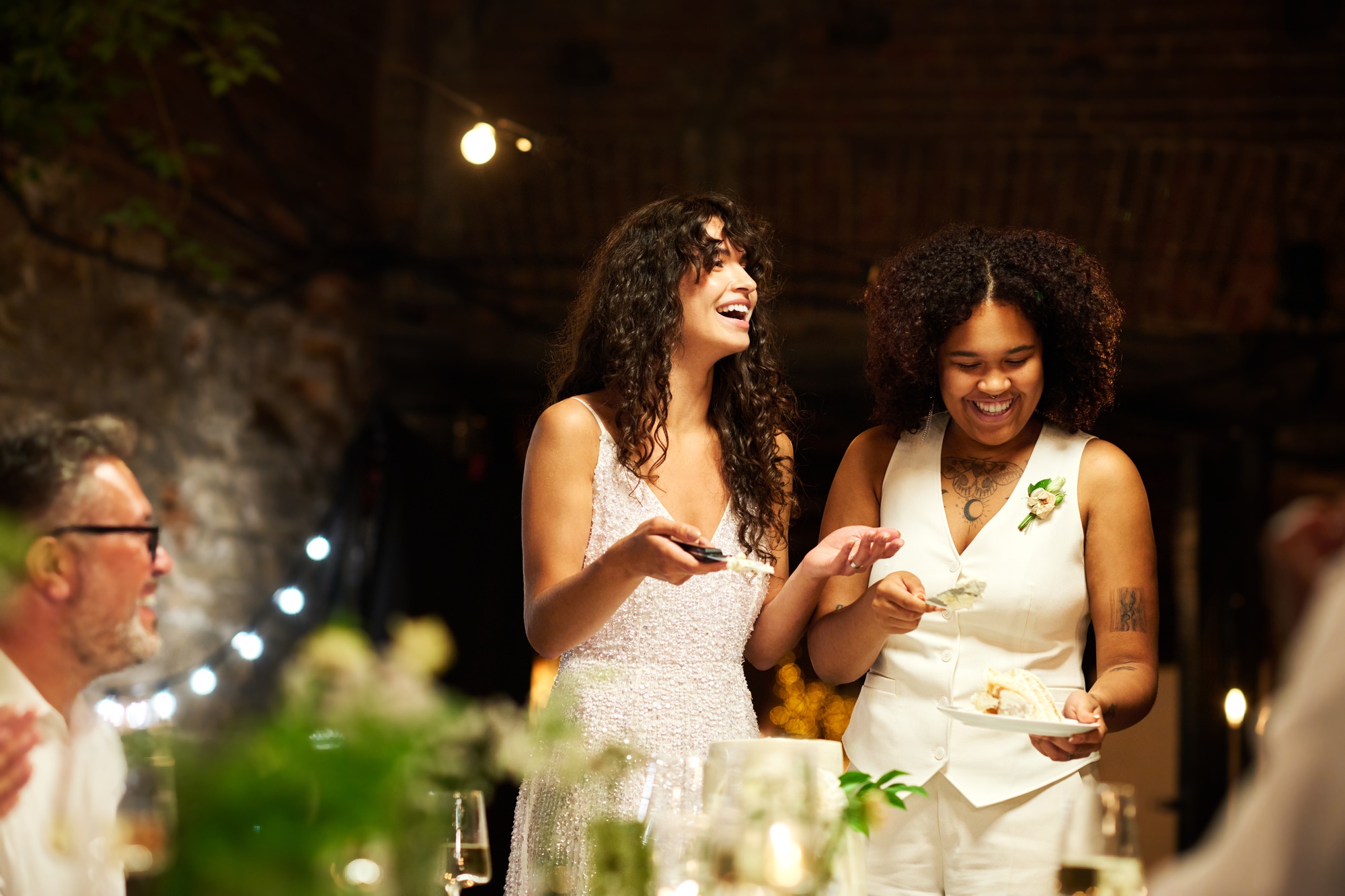Cheerful young lesbian brides in wedding attire spreading cake among guests
