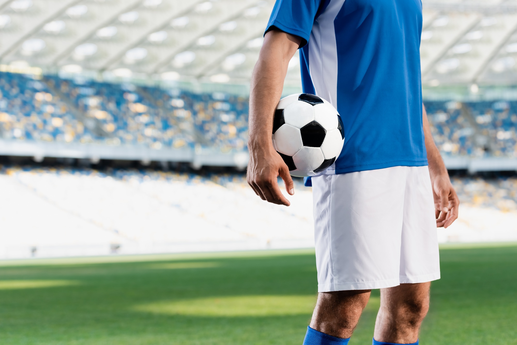 cropped view of professional soccer player in blue and white uniform with ball on football pitch at