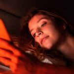 Young girl with smartphone in a bed. Red illumination
