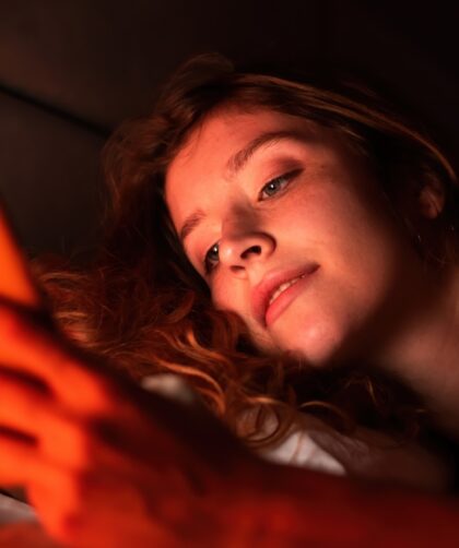 Young girl with smartphone in a bed. Red illumination
