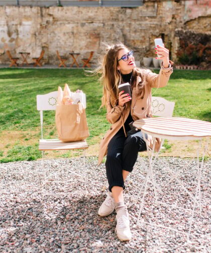 Attractive hipster girl wearing beige coat makes selfie for instagram profile during coffee break in